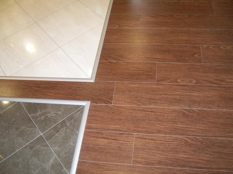 Połączenie trzech rodzajów podłóg: jasne płytki kwadratowe ułożone romboidalnie, ciemne płytki imitujące marmur ułożone romboidalnie oraz panele podłogowe imitujące drewno, wszystkie wykończone...