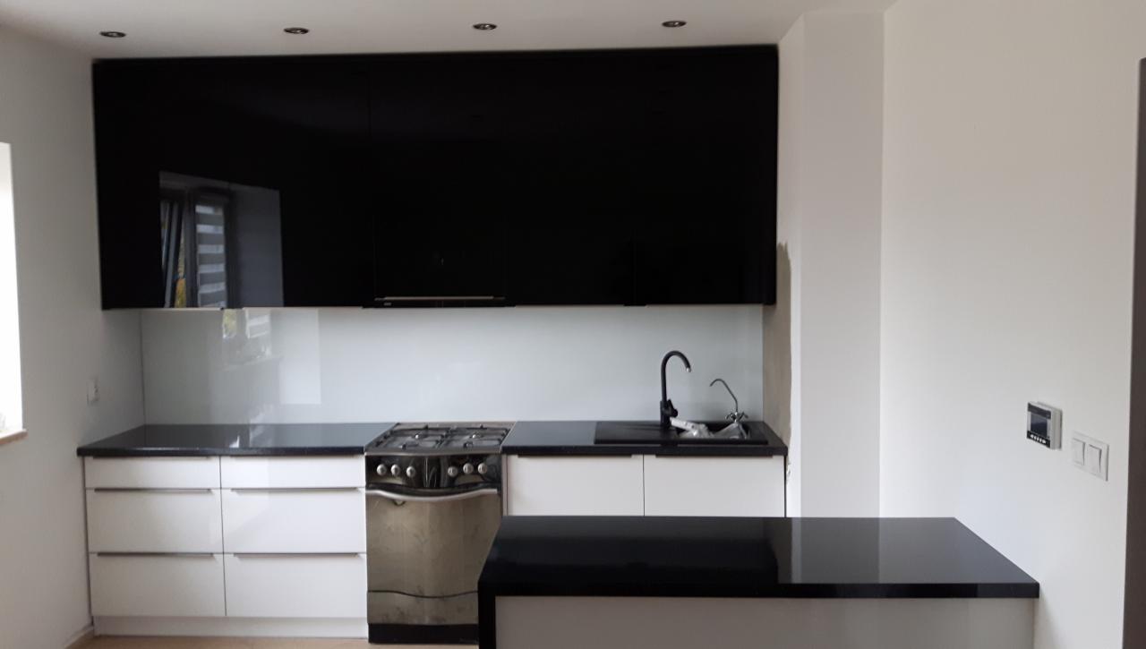 Nowoczesna kuchnia z czarnymi szafkami górnymi na wysoki połysk, białymi szafkami dolnymi z szufladami, czarnym blatem i płytą gazową ze srebrnym piekarnikiem.