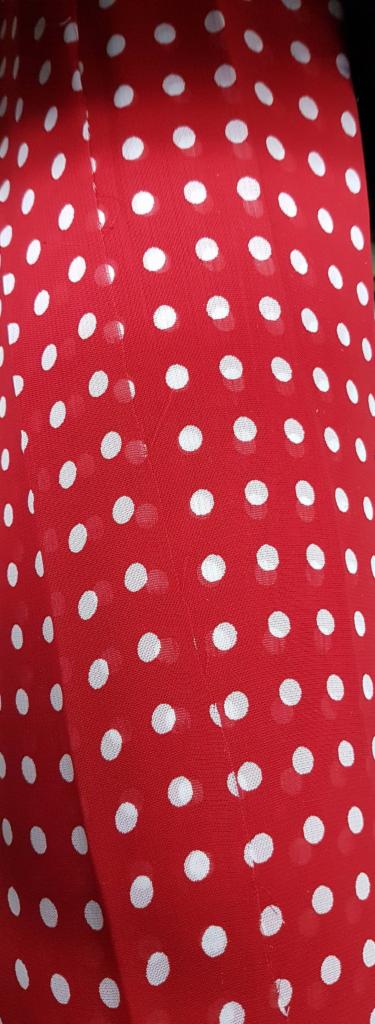 Czerwona, półprzezroczysta tkanina w białe kropki, widoczne delikatne zagniecenia i faktura materiału.