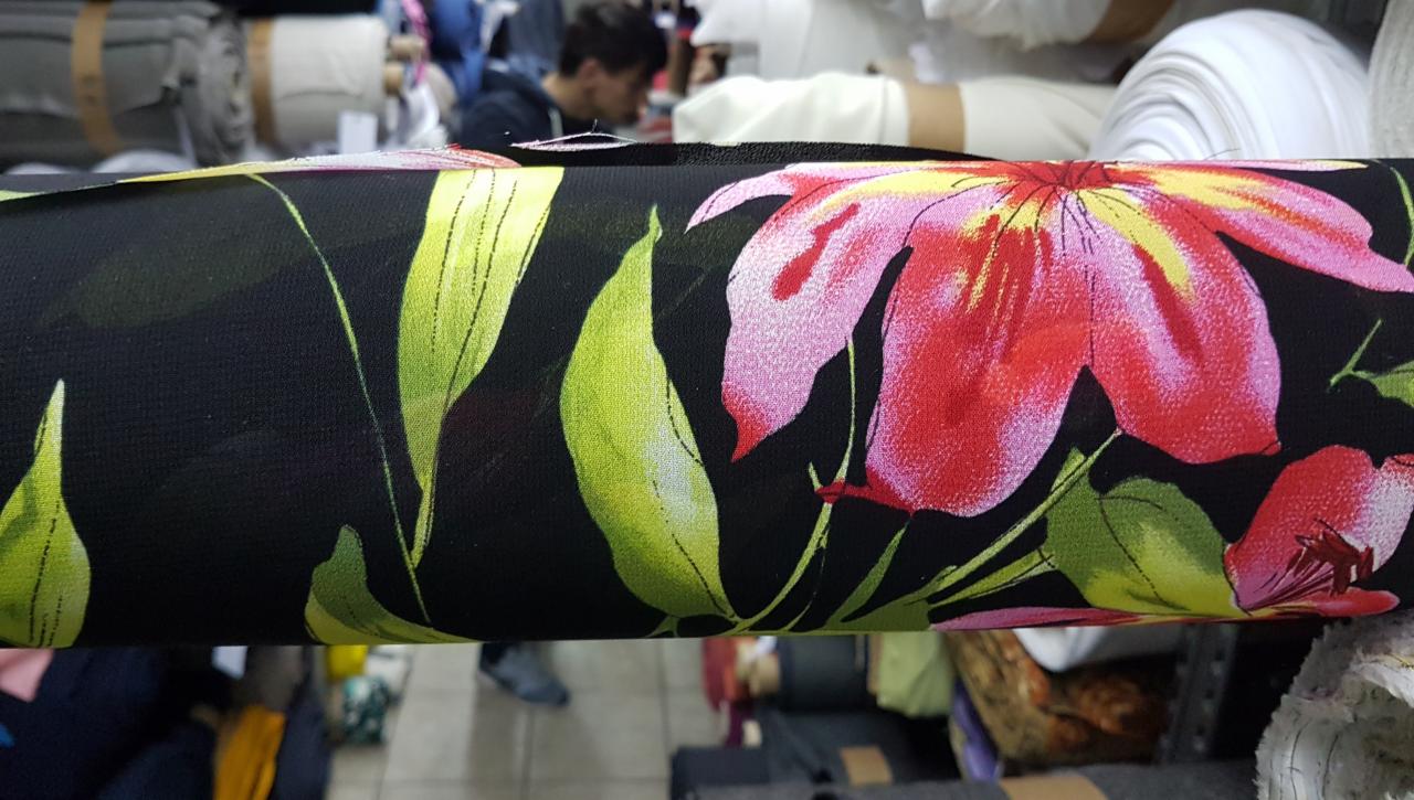 Rolka czarnej tkaniny w kwiaty z wyraźnym wzorem czerwono-różowych kwiatów i zielonych liści, prezentowana w hurtowni w Warszawie.