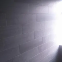 Ściana w łazience wyłożona szarymi, podłużnymi płytkami imitującymi drewno, z widocznymi elementami instalacji wodnej i silnym światłem w rogu.