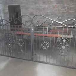 Wykute z metalu dwuskrzydłowe ogrodzenie z ozdobnymi elementami, w warsztacie na tle ceglanej ściany i drabiny.