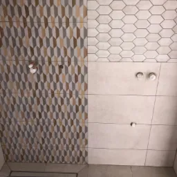 Różnorodność wzorów płytek w łazience: geometryczne romby w odcieniach szarości i brązu, heksagonalne płytki oraz gładkie, beżowe powierzchnie, widoczne przyłącza wodne i odpływ liniowy.