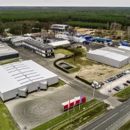 Widok z lotu ptaka na zakład produkcyjny z magazynami, składowiskiem agropelletu w workach i parkingiem dla pracowników.