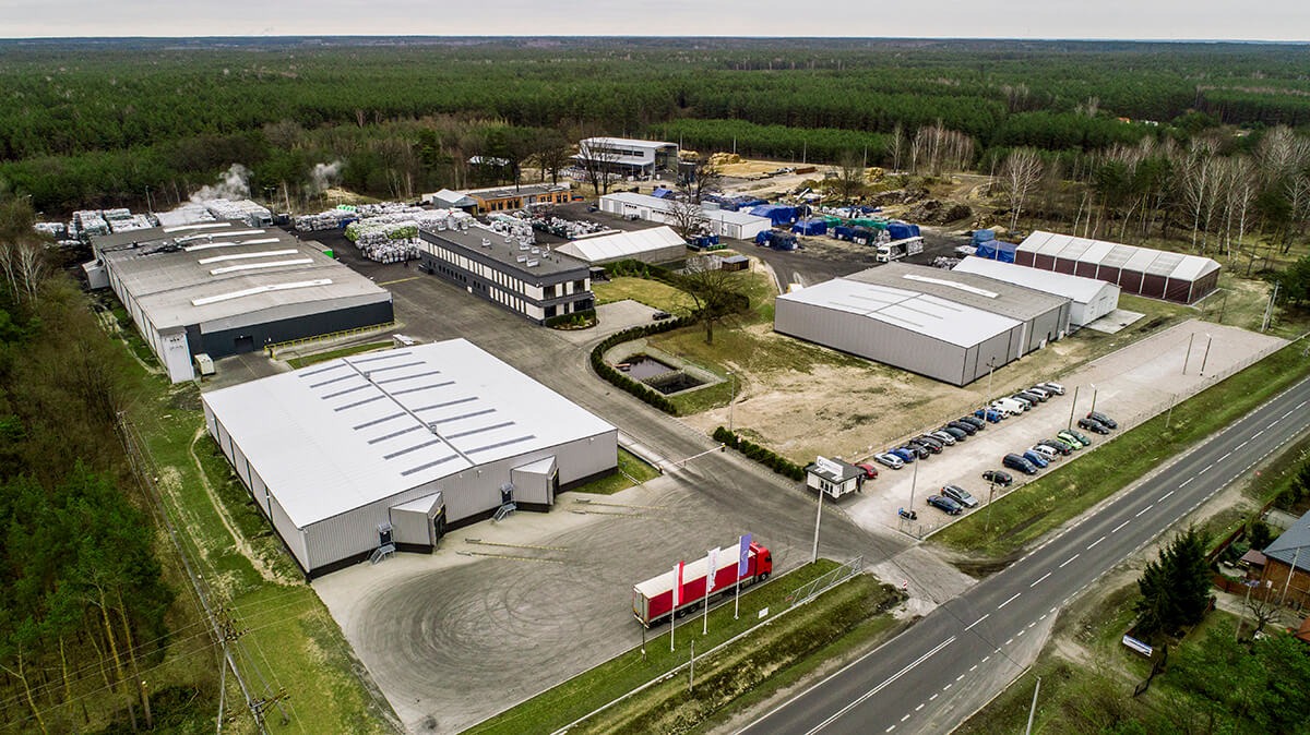 Widok z lotu ptaka na zakład produkcyjny z magazynami, składowiskiem agropelletu w workach i parkingiem dla pracowników.