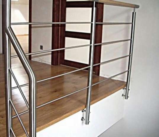 Schody z drewnianymi stopniami zabezpieczone metalową barierką z poziomymi prętami i drewnianym uchwytem, widok z dołu.