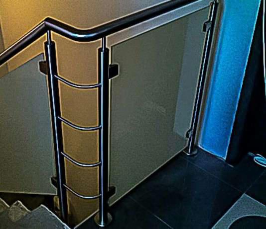 Szklana balustrada schodowa z metalowymi elementami mocującymi i poręczą, widok z góry na fragment schodów.