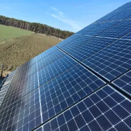 Panel słoneczny na dachu domu, z widokiem na zielone pole i las w tle, sfotografowany w słoneczny dzień. Detaliczna instalacja fotowoltaiczna.