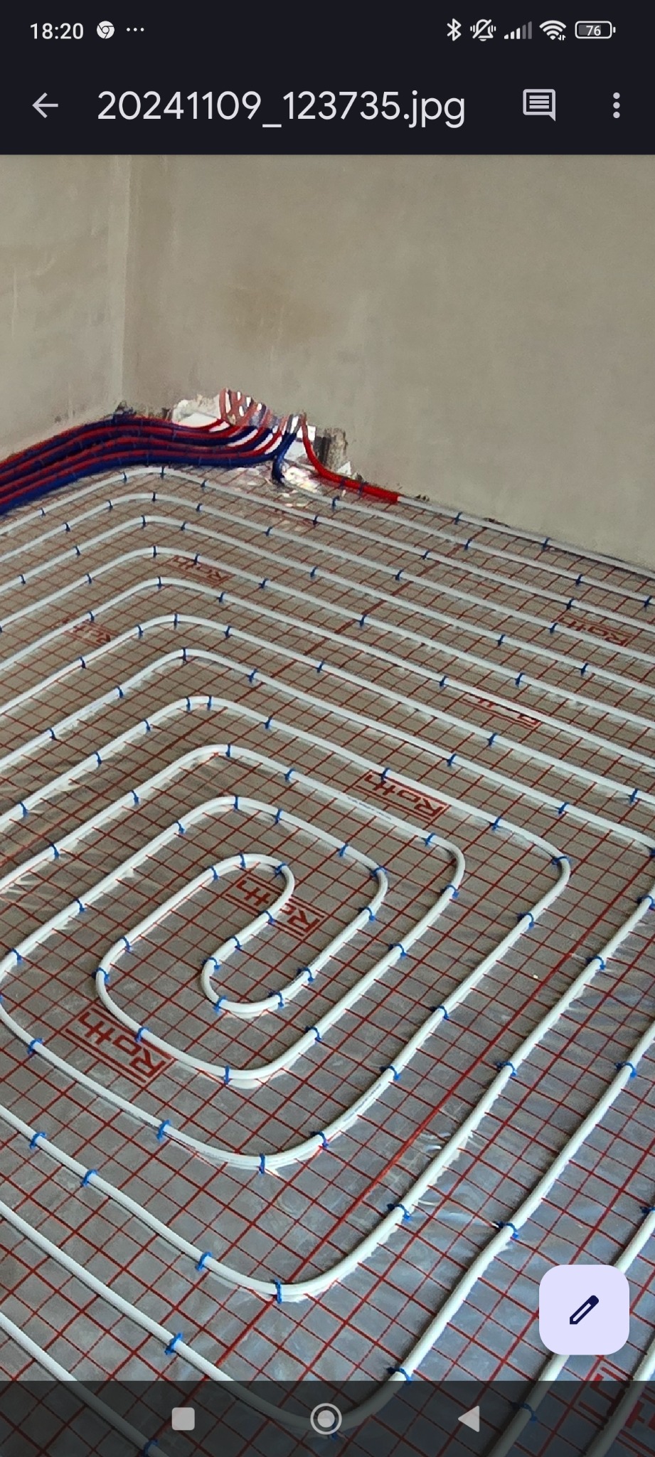 Układanie białych rur grzewczych na siatce z czerwonymi liniami, mocowanych niebieskimi klipsami, przygotowywane do wylewki na ogrzewanie podłogowe.