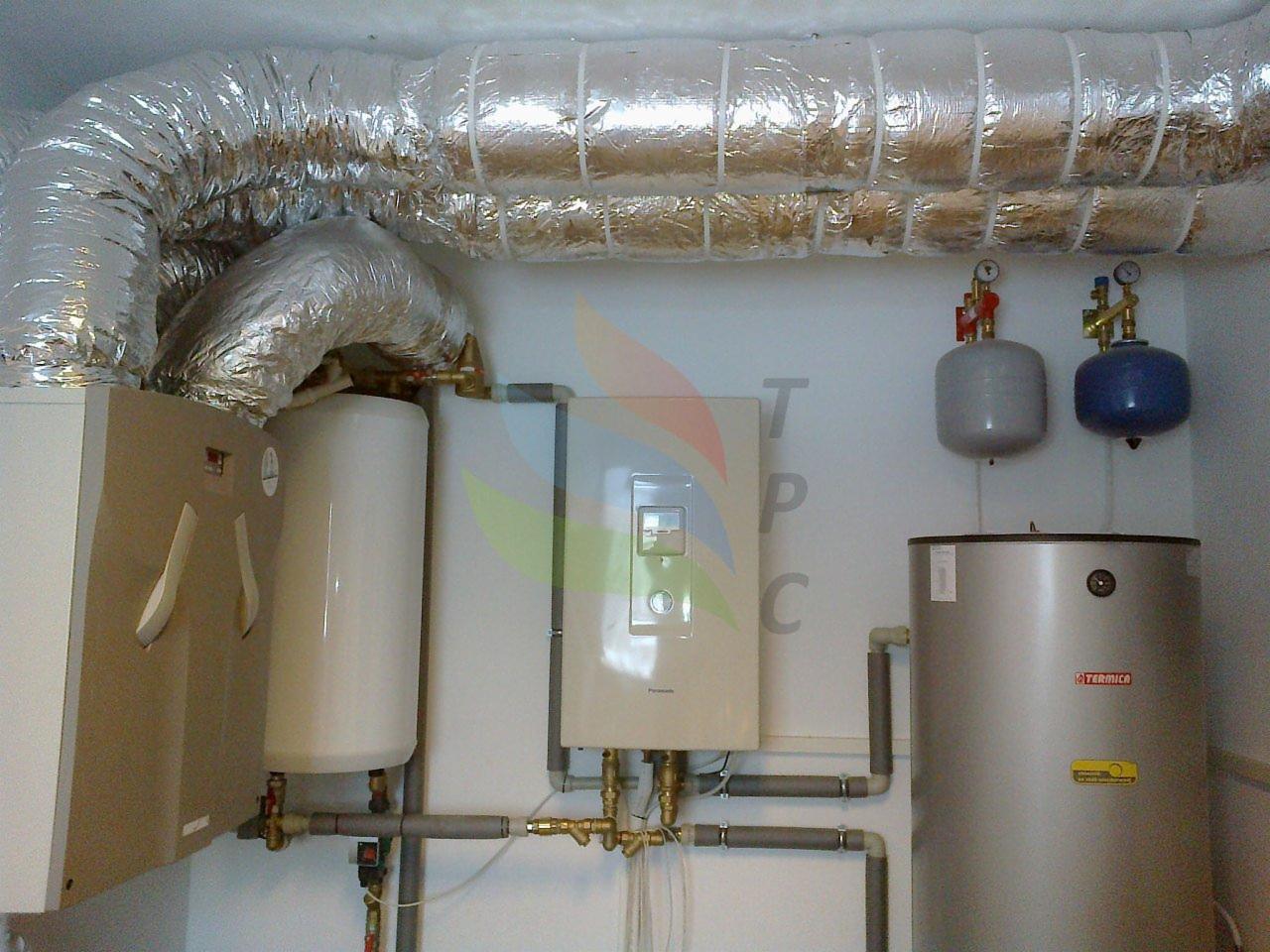 Zestaw urządzeń grzewczych w kotłowni: piec gazowy, zasobnik ciepłej wody, naczynia przeponowe i izolowane przewody wentylacyjne pod sufitem.