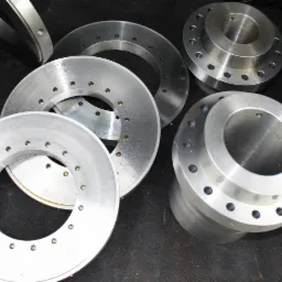 Metalowe, okrągłe elementy z otworami, wykonane z dbałością o detal. Różne rozmiary i kształty na ciemnym tle. Precyzyjna obróbka materiałów.