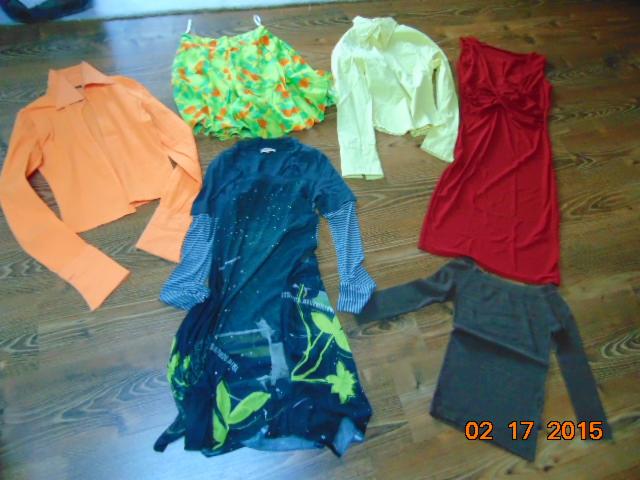 Kolekcja odzieży używanej: pomarańczowa bluzka, wzorzysta spódnica, żółta koszula, czerwona sukienka i tunika z długim rękawem na drewnianej podłodze.