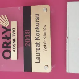 Tablica z logo 'Orły Kosmetyki 2018 Laureat Konkursu Wybór Klientów' oraz certyfikat 'La Femme' Elżbieta Sadlik na różowym tle.
