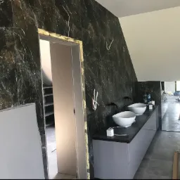 Remont łazienki na poddaszu: czarne marmurowe płytki, białe umywalki nablatowe, szara szafka pod umywalką, montaż drzwi przesuwnych z pianką montażową, widoczne przewody.