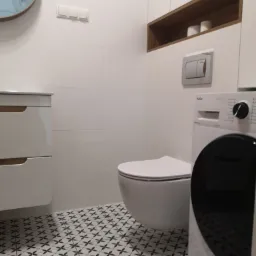 Nowoczesna łazienka z białą armaturą, wzorzystą podłogą i pralką marki Amica.