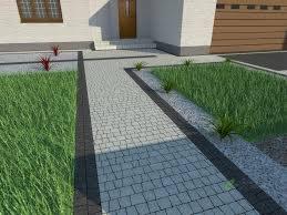 Ścieżka z szarej kostki brukowej ułożona wzdłuż trawnika i białego domu z brązowymi drzwiami, obrzeża z ciemnej kostki, dekoracyjne rośliny.