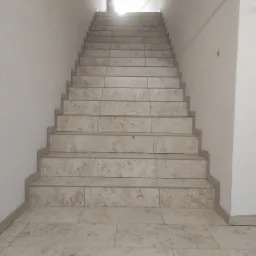 Wykończone schody wewnętrzne w Sińcach, wyłożone jasnymi, beżowymi płytkami imitującymi kamień, z widocznymi fugami i oświetleniem z góry.