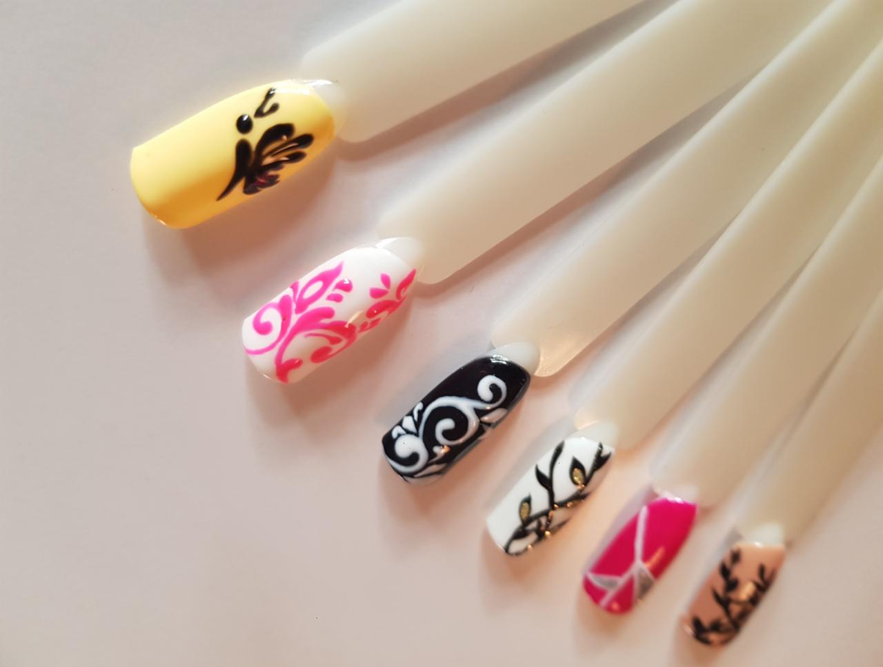 Wzornik z sześcioma sztucznymi paznokciami, każdy pomalowany innym, ozdobnym wzorem: żółty z czarnym motywem roślinnym, biały z różowym ornamentem, czarny z białymi zawijasami, biały z złotymi...
