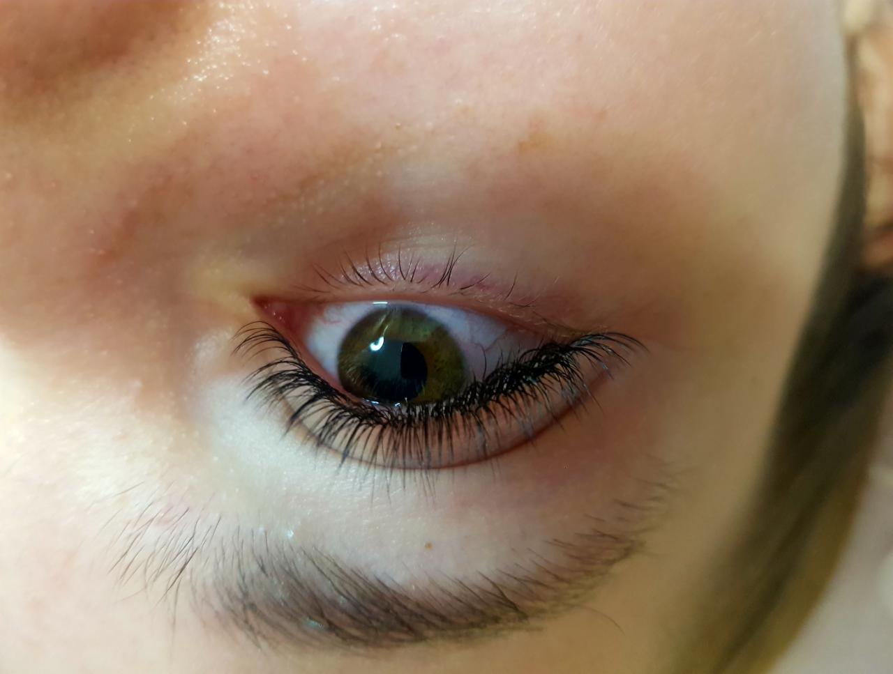 Zbliżenie na oko z wyraźnie przedłużonymi, czarnymi rzęsami, widoczne delikatne włoski brwi i zielona tęczówka.