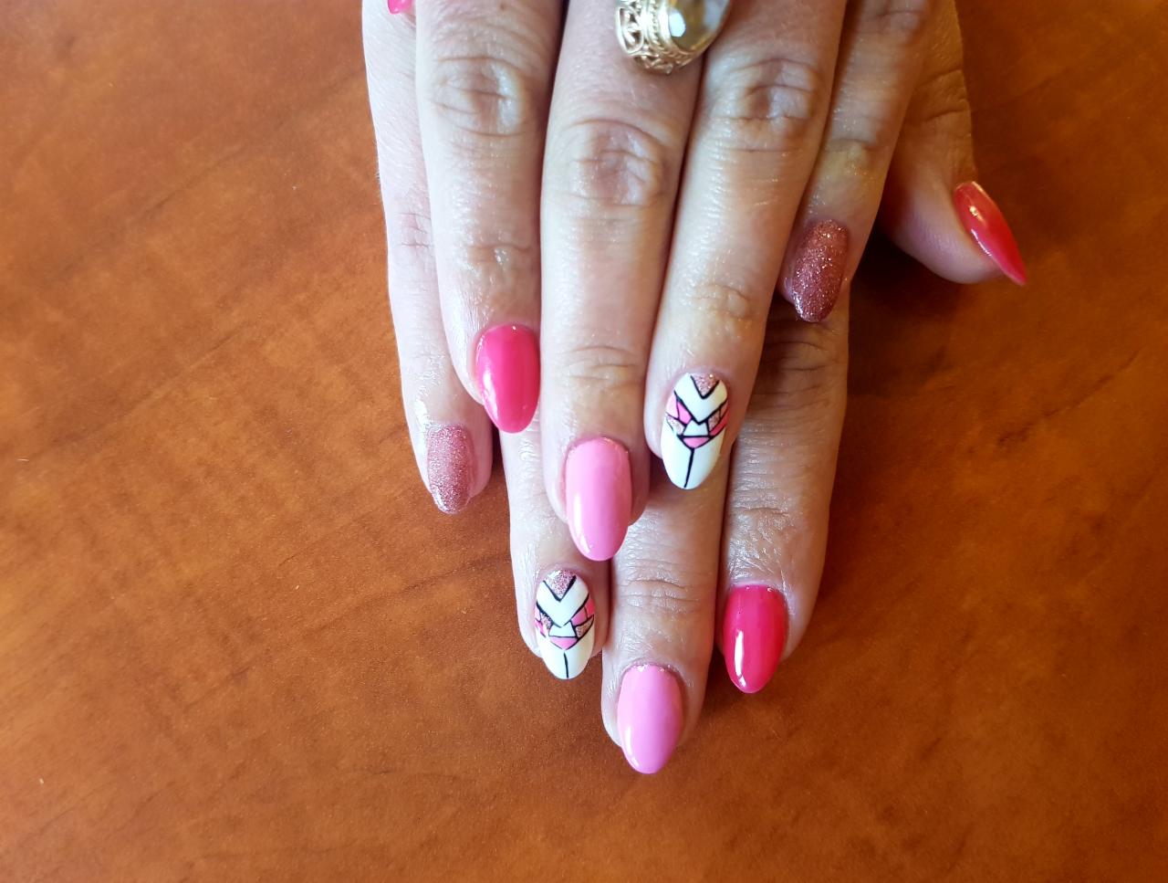 Ręka z różnymi stylami manicure: różowe, brokatowe i białe paznokcie z geometrycznym wzorem w kolorze różowym i czarnym, ozdobny pierścionek na serdecznym palcu.