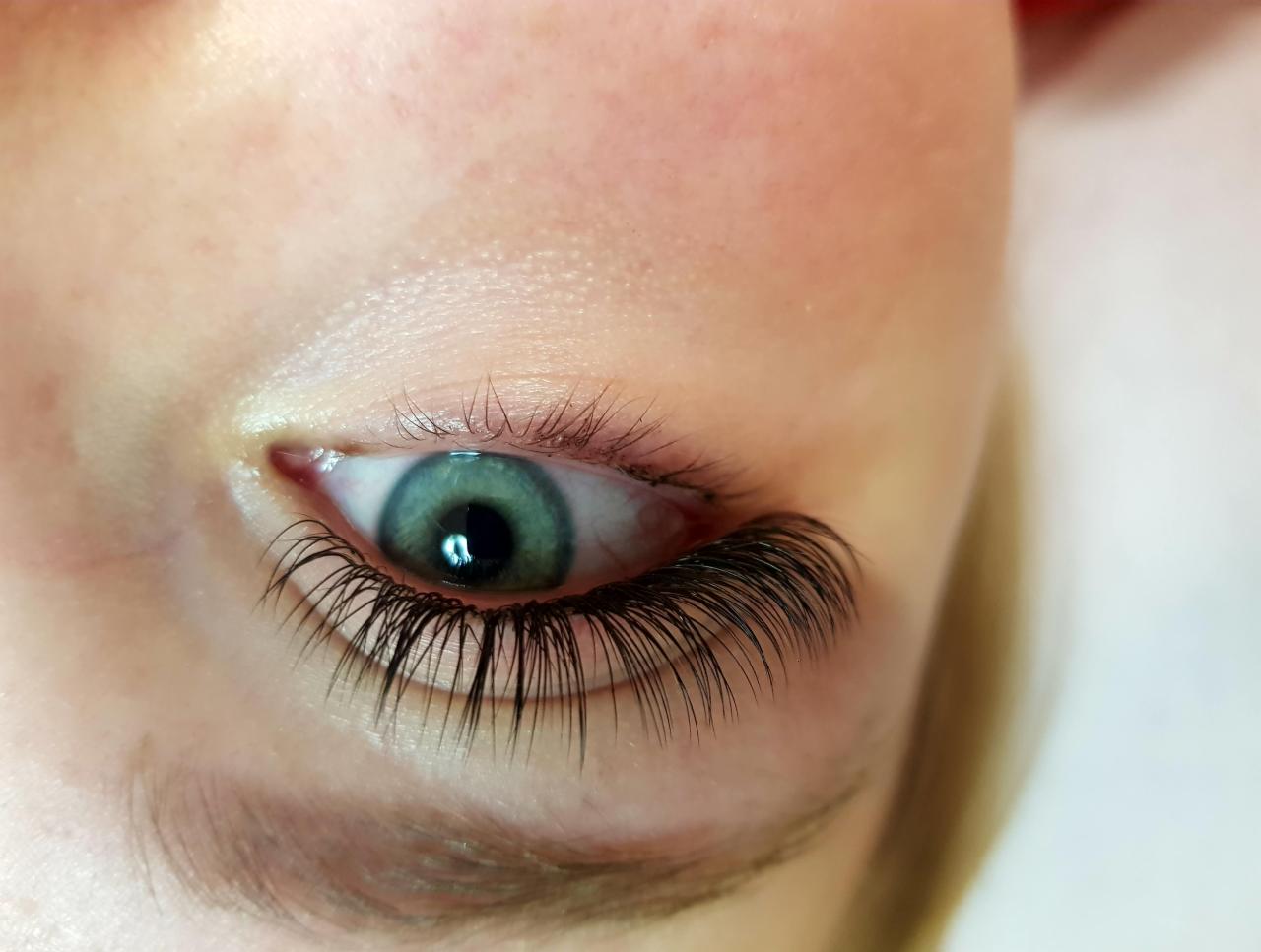 Zbliżenie na oko z przedłużonymi, gęstymi rzęsami; widoczny odrost naturalnych rzęs i delikatny zielony kolor tęczówki.