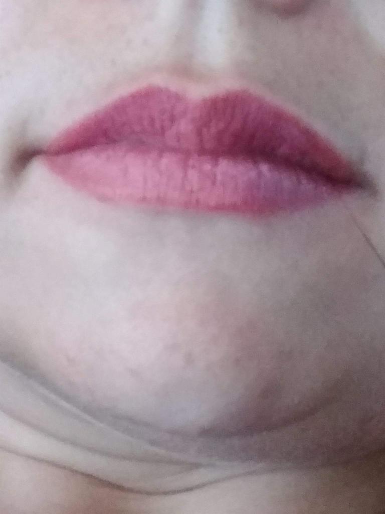 Zbliżenie na usta z pomalowanymi na różowo wargami, widoczne lekkie niedoskonałości cery.