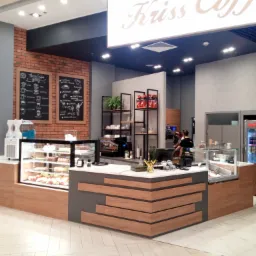 Nowoczesna aranżacja wnętrza kawiarni z drewnianymi elementami zabudowy, ekspozycją ciast i napojów, oraz tablicami kredowymi z menu.