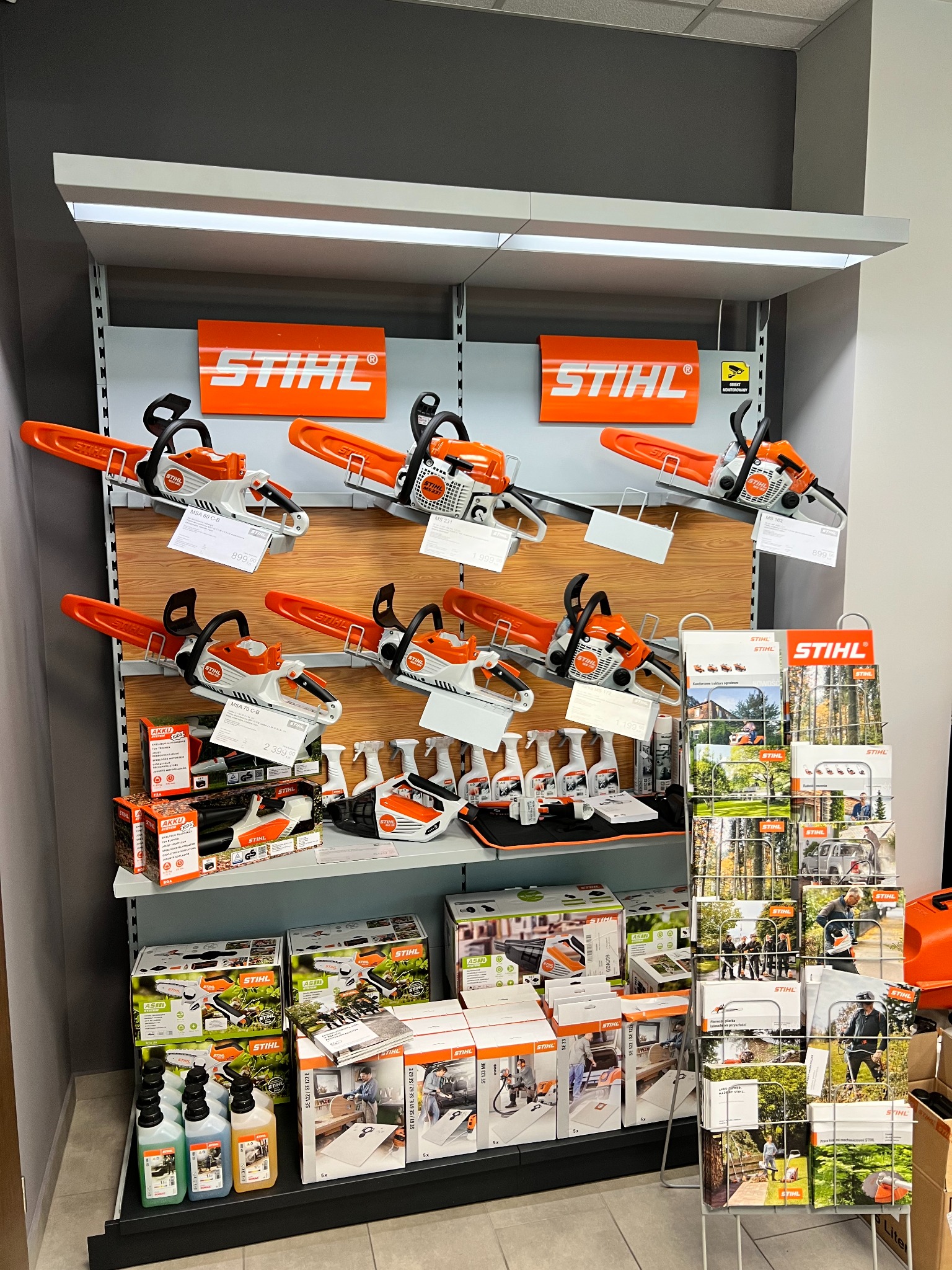 Ekspozycja w sklepie z elektronarzędziami Stihl: rzędy pilarek łańcuchowych, dmuchaw, olejów i katalogów na półkach.