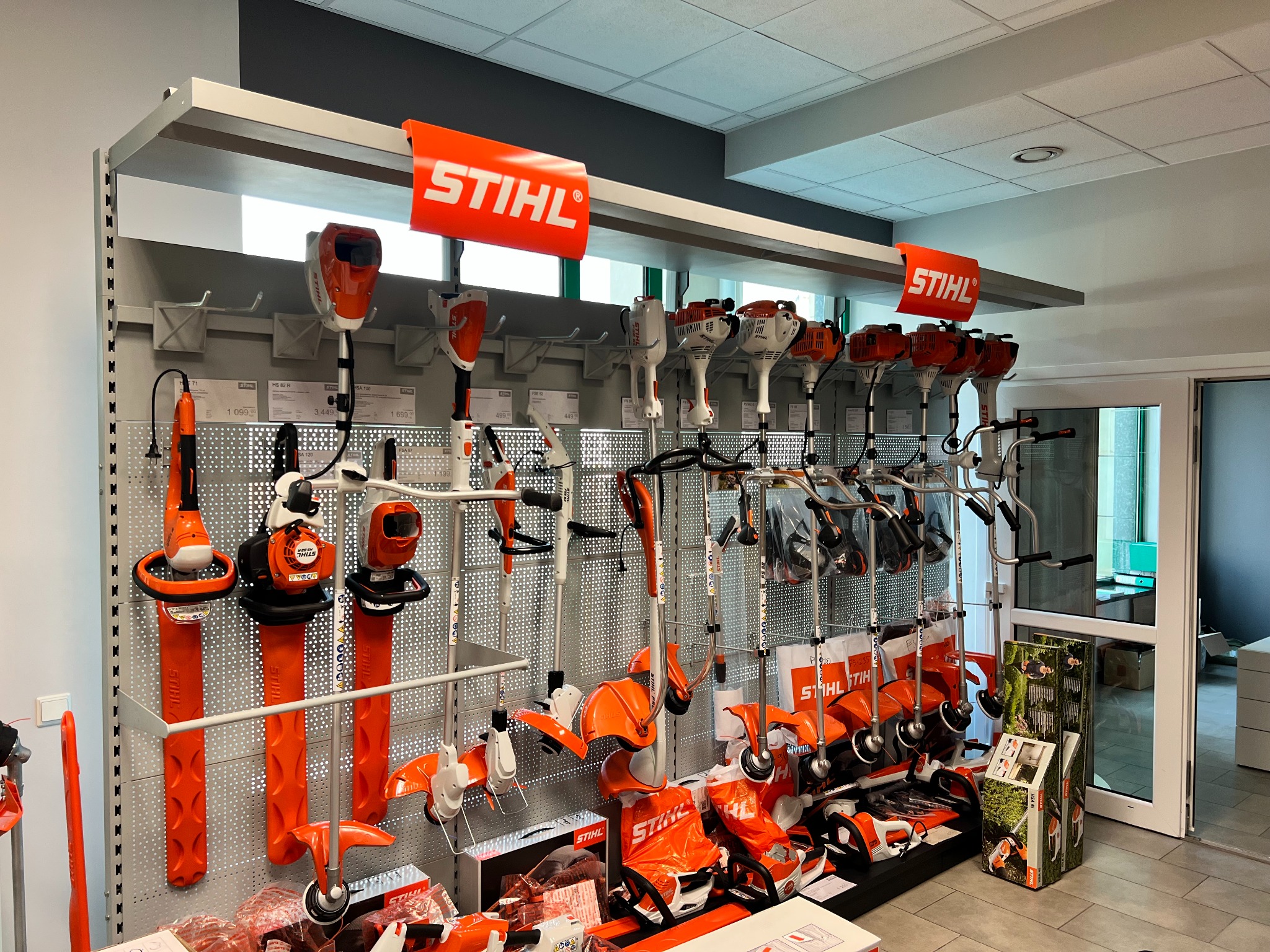 Ekspozycja w sklepie z elektronarzędziami Stihl, prezentująca różnorodność kos spalinowych i elektrycznych, nożyc do żywopłotu i innych urządzeń ogrodniczych, z wyraźnym brandingiem marki.