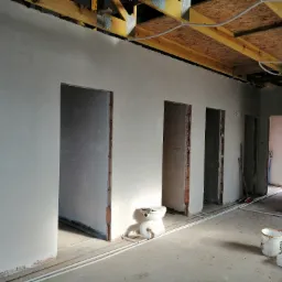 Świeżo położone, jasne ściany w surowym stanie budynku w Gnieźnie, z widocznymi otworami drzwiowymi i fragmentem instalacji pod sufitem.
