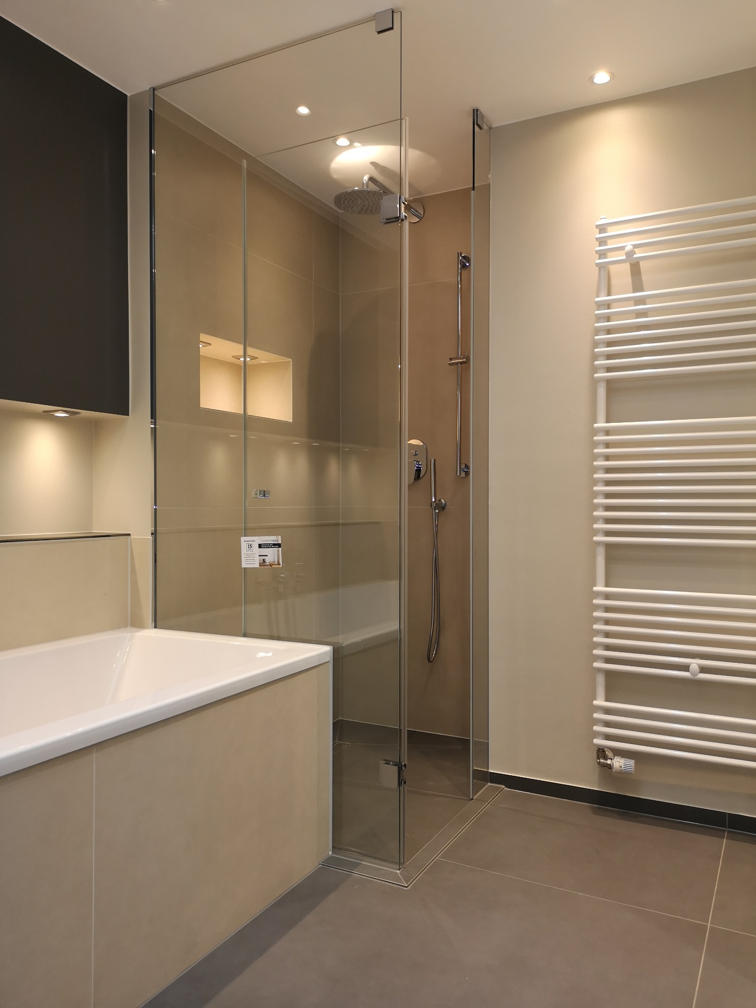 Nowoczesna łazienka z kabiną prysznicową typu walk-in, grzejnikiem drabinkowym i podświetlaną wnęką w ścianie.