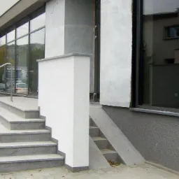 Zewnętrzne schody wejściowe do budynku z szarych płyt granitowych, z metalową balustradą, widok z boku.