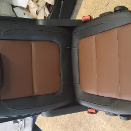 Dwa odnowione fotele samochodowe z brązową tapicerką na środku i czarną skórą po bokach, widoczne czerwone elementy pasów bezpieczeństwa.