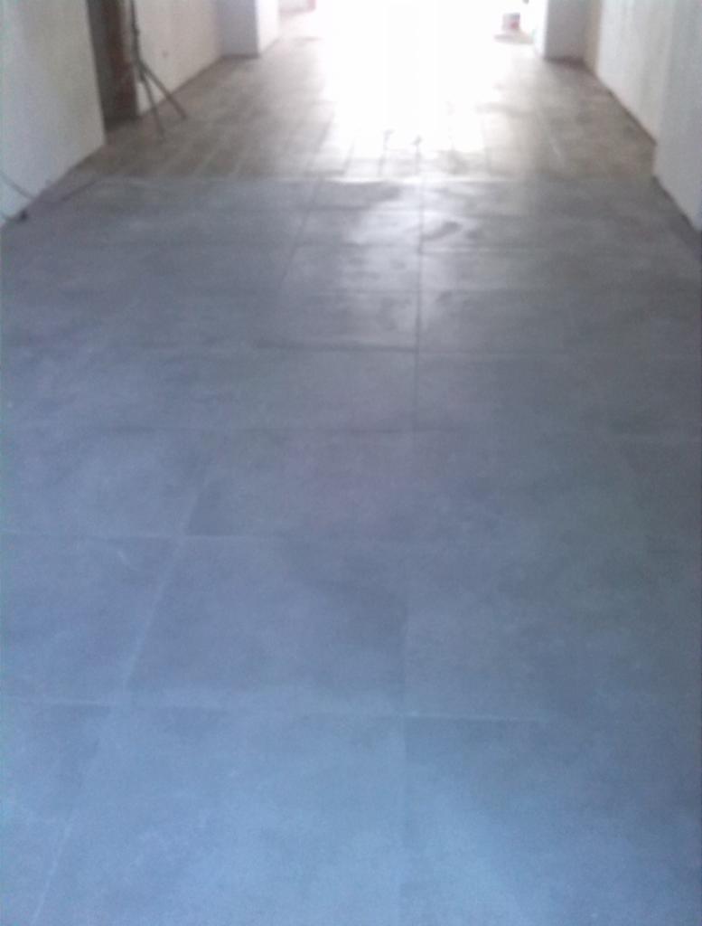 Wyrównana, szara posadzka z płyt wewnątrz budynku w Tchórzew-Kolonia, z widocznymi fugami i rozproszonym światłem w tle, ukazująca efekt niwelacji podłoża.