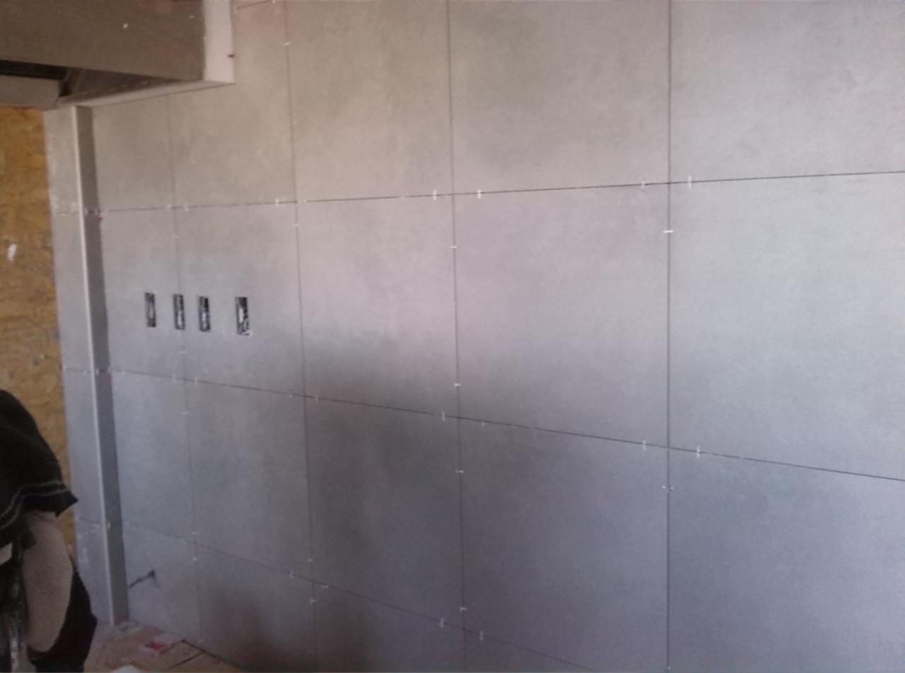 Ściana w trakcie tynkowania z widocznymi liniami podziału i plastikowymi krzyżykami dystansowymi, przygotowana pod gładź, z widocznymi puszkami elektrycznymi.