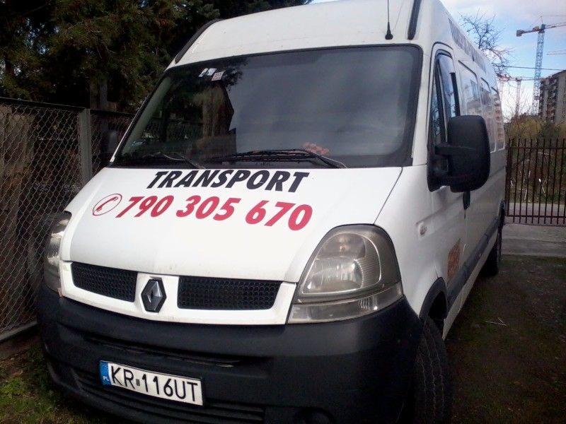 Biały Renault Master z napisem 'TRANSPORT' i numerem telefonu 790 305 670, zaparkowany przy ogrodzeniu z siatki, w tle widoczny budynek w budowie i żuraw.