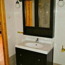 Sab-Bud - Ciemna szafka łazienkowa z umywalką i lustrem w drewnianej ramie, oświetlona kinkietami, na tle ściany wyłożonej mozaiką.