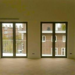 Sab-Bud - Jasne, przestronne wnętrze z trzema balkonami i widokiem na budynki z cegły; świeżo pomalowane ściany i jasna podłoga tworzą minimalistyczny efekt.