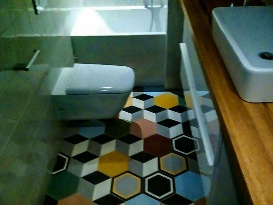 Wnętrze łazienki z toaletą, umywalką i wanną, wyróżniające się podłogą z kolorowych, geometrycznych płytek w kształcie sześcianów.