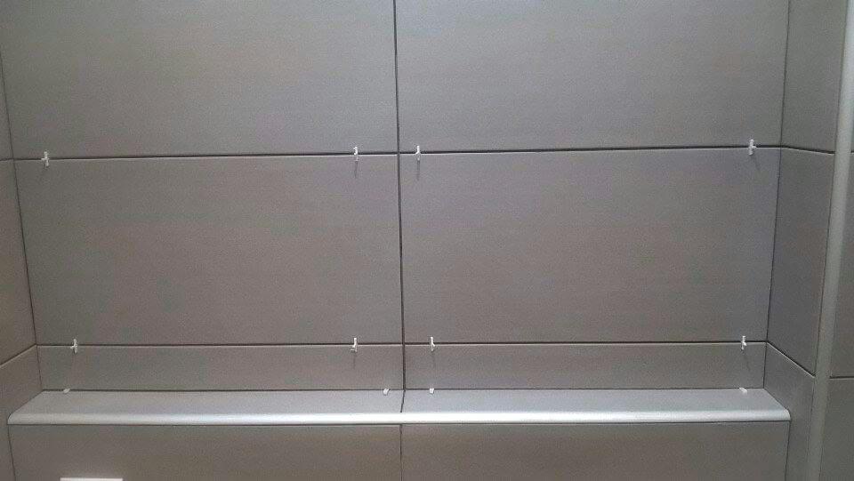 Świeżo położone, szare płytki ceramiczne w łazience, widoczne krzyżyki dystansowe, minimalistyczny design.