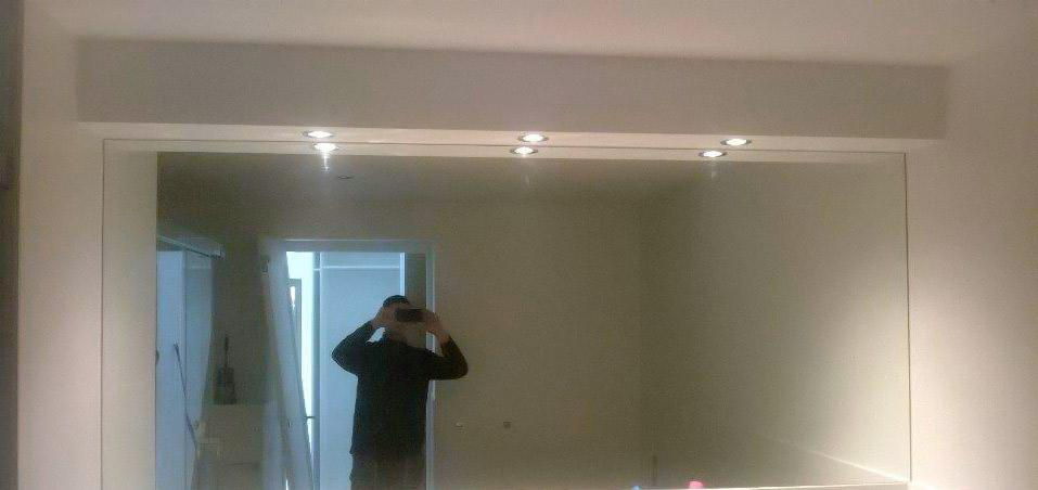 Zamontowane duże lustro na ścianie z oświetleniem punktowym w suficie podwieszanym, odbicie osoby robiącej zdjęcie.