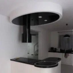 Nowoczesny sufit podwieszany z okrągłą, czarno-białą konstrukcją nad wyspą kuchenną i zamontowanym okapem. Widoczne trzy punktowe źródła światła w czarnej części sufitu.