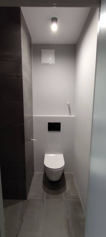 Nowoczesna, minimalistyczna toaleta z podtynkową spłuczką, szarą glazurą i podświetlanym sufitem.