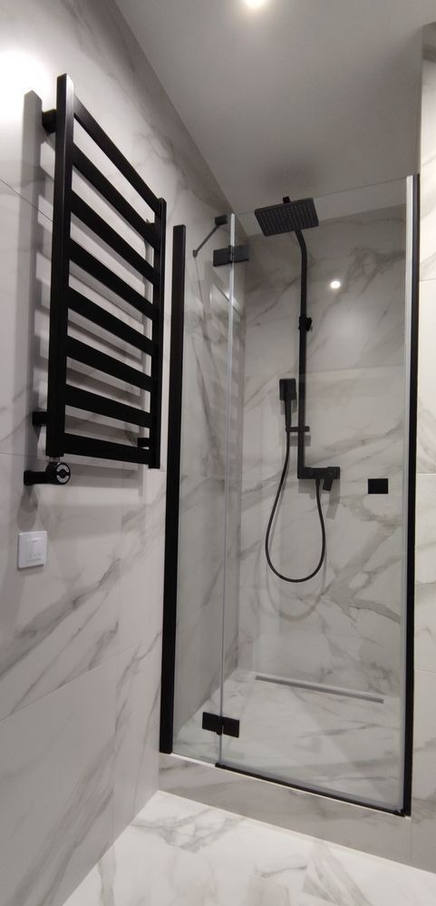 Nowoczesna kabina prysznicowa z czarnymi elementami, grzejnik drabinkowy w tym samym kolorze na tle marmurowych płytek.