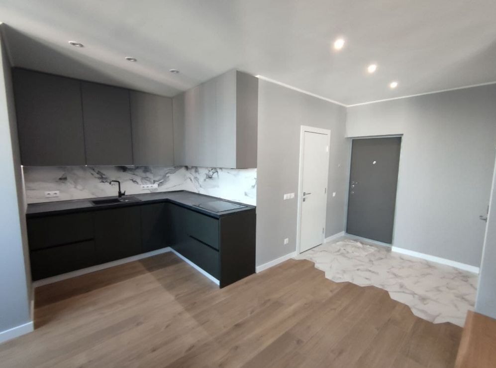 Nowoczesna kuchnia w odcieniach szarości z marmurowym panelem nad blatem, drewnopodobne panele na podłodze, widoczne przygotowania do położenia płytek w przedpokoju.