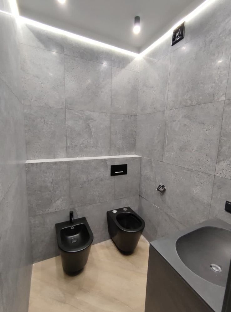 Nowoczesna łazienka z szarymi płytkami imitującymi beton, czarną armaturą (bidet i toaleta) oraz podświetleniem LED podsufitowym.