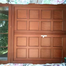 Duże, dwuskrzydłowe drzwi wejściowe z drewna z szybą boczną, widoczne ślady graffiti na ścianie i posadzce, wiadro z narzędziami w rogu.