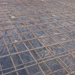 Zbrojenie z prętów stalowych ułożone na czarnej folii, przygotowane do wylania betonu, z widocznym dystansem z kostki betonowej.