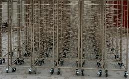 Stojaki z metalowej siatki na kółkach, ustawione w rzędzie, widoczne liczne spawy i łączenia elementów siatki.