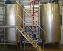 Dwa duże, metalowe zbiorniki przemysłowe połączone rurami i schodami. Widoczne zawory i elementy instalacji.
